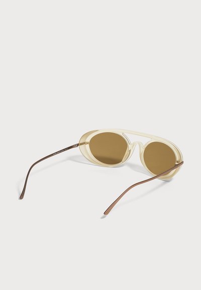 Lunettes de soleil ovales avec des montures translucides beige clair et des branches fines marron, vues de dos sur fond blanc.