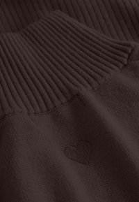 Bruine trui met een ribgebreide halslijn en een zachte textuur, met een klein geborduurd hartdetail nabij de zoom.