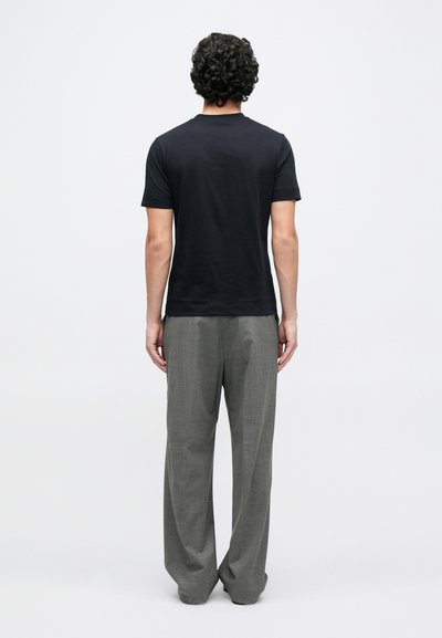 Juoda trumpomis rankovėmis marškinėliai derinami su šviesiai pilkais, laisvo silueto kelnėmis, matomi iš nugaros. Audinys lygus su švelniu blizgesiu.