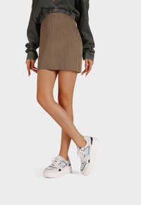 Gonna a coste beige abbinata a sneakers con plateforme bianche e azzurre chiare, con dettagli di cucitura e lacci. Texture del tessuto morbida visibile.