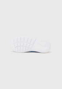 Semelle de basket blanche avec un motif de grip texturé, présentant des bords arrondis et un logo discret; conçue pour la traction et le confort.