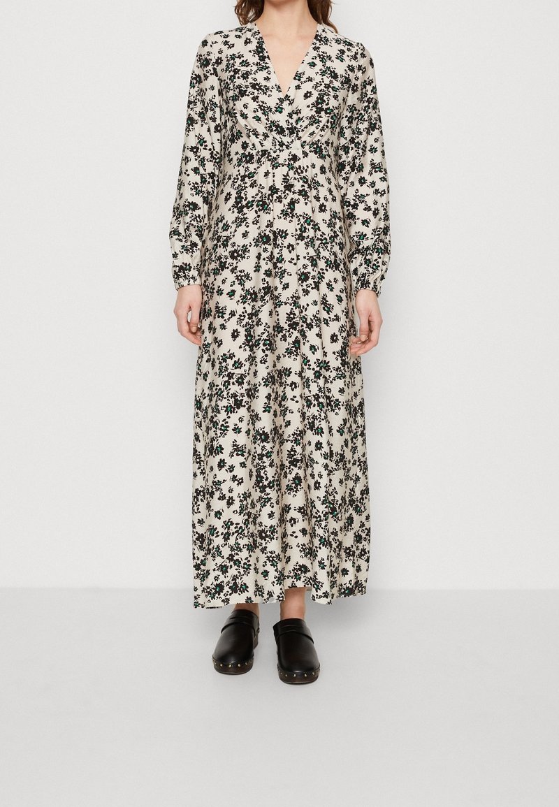Robe longue florale avec un décolleté en V profond, des manches longues et une base beige. Présente des motifs floraux noirs et verts ; portée avec des sabots noirs.