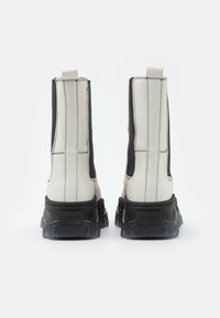 Botas de tobillo blancas y negras con una suela de goma gruesa, que presentan paneles elásticos en los costados, costuras blancas y un tacón con marca.