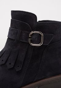 Suedesko med ankellängd i mörk marinblått med rundad tå. Har en sidospänne och fransdetaljer. Den släta texturen och de stickade detaljerna förhöjer designen.