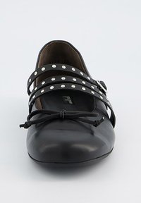 Zapato de cuero negro con punta redondeada, presenta tres correas paralelas adornadas con tachuelas plateadas y un lazo decorativo en la parte delantera.