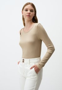 Beige Struktur-Longsleevetop mit runden Ausschnitt, kombiniert mit hoch geschnittenen weißen Jeans und einem Zweiknopfdetail an der Taille.