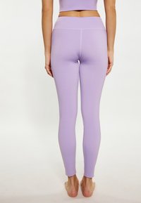 Lila leggings, sima textúrával és magas derékkal. Egyszerű dizájnnal rendelkezik, és szorosan illeszkedik, egészen a bokaig terjed.