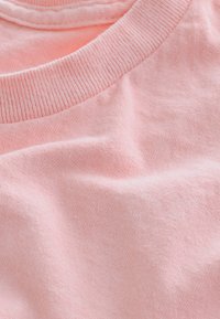 Bleekroze katoenen T-shirtstof met een geribbelde ronde hals, met een zachte textuur en een lichte glans, met subtiele variaties.