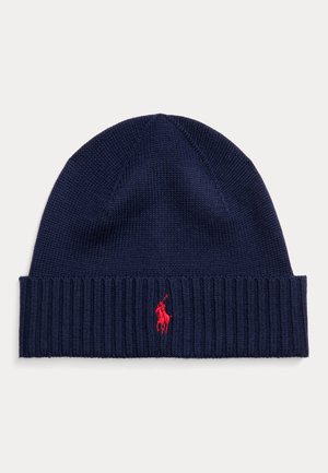 Gorro de malha azul-marinho com punho canelado, apresentando um pequeno logo vermelho da polo de lado. Textura suave e design ajustado.