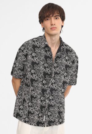 Camisa negra de manga corta con un patrón floral blanco, diseño abotonado, corte relajado y textura suave.