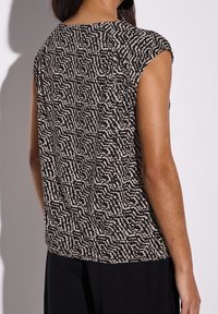 Černý a krémový vzorovaný top s krátkými rukávy, který se vyznačuje texturovaným vlnitým designem. Zadní strana má uvolněný střih a kulatý výstřih.