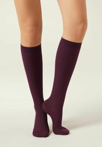 Calzini al ginocchio in un profondo colore bordeaux, con texture a coste verticali e polsino rinforzato per una vestibilità sicura. Finitura liscia su tutta la superficie.