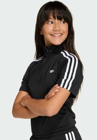 Czarna sportowa bluzka z wysokim kołnierzem i pół-zamkiem, zdobiona białymi paskami na rękawach oraz małym logo na klatce piersiowej.