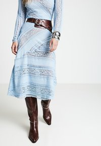 Robe en dentelle bleu clair à manches longues, motifs superposés, ceinturée d'une ceinture en cuir marron. Des bottes marron pointues montantes jusqu'aux genoux complètent la tenue.