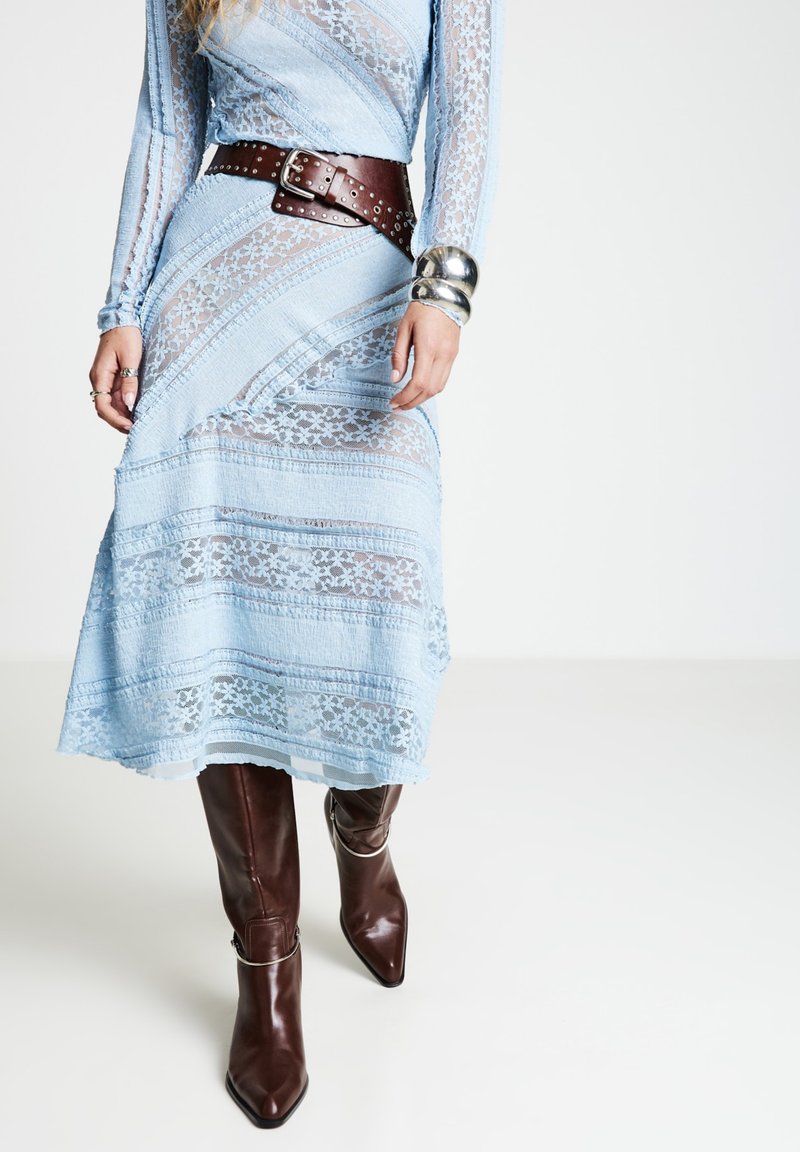 Robe en dentelle bleu clair à manches longues, motifs superposés, ceinturée d'une ceinture en cuir marron. Des bottes marron pointues montantes jusqu'aux genoux complètent la tenue.