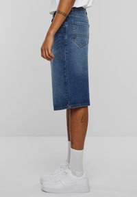 Sininen denim-midi hame, jossa on suora leikkaus, takataskut ja joka on yhdistetty valkoisiin lenkkareihin ja harmaisiin sukkiin.