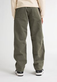Relaxed-fit olijfgroene broeken, met achterzakken en een stevige textuur, gecombineerd met zwart-witte sportschoenen.