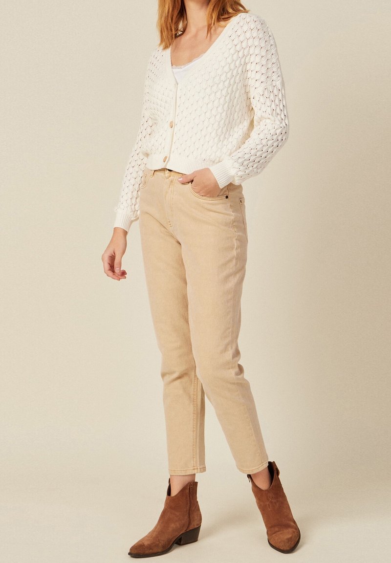 White knitted cardigan with a honeycomb pattern, paired with beige straight-leg jeans and brown ankle boots with a low heel.