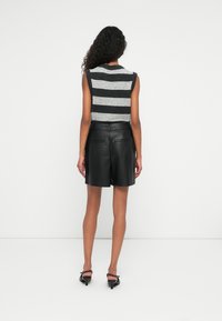 Särgideta hall ja must triibuline topp, millele on sobitatud kõrge vöökohaga mustad nahkpüksid. Sile tekstuur, minimalistlik kujundus ja peened taskud.