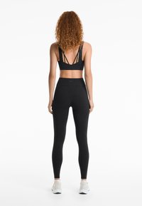 Bralette de sport noir avec un design à plusieurs bretelles à l'arrière, associé à un legging noir taille haute, le tout en tissu lisse et extensible.