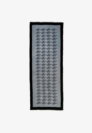 Gråt sjal med hundetandmønster, frynsete kanter og ensfarvet sort kant. Båret over en mørk top og skinnende sorte læderbukser.