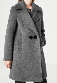 Grijze wollen jas met een zachte, gestructureerde afwerking, een notched kraag, een dubbelbreasted ontwerp en twee grote zwarte knopen. Voorzien van zijzakken.