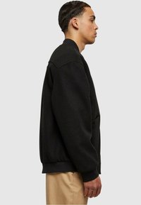Sudadera negra de corte relajado, con cuello redondeado y puños acanalados. Cuenta con bolsillos laterales, fabricada en un tejido suave y texturizado.