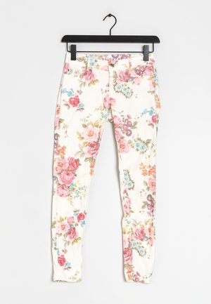 Jean à imprimé floral avec un fond blanc, des fleurs roses, bleues et vertes, en denim et au design ajusté. Accroché à un cintre noir.