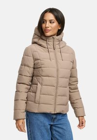 Beige gewatteerde jas met een afneembare capuchon, zichtbare stiknaden, ritssluiting aan de voorkant en verstelbare trekkoorden. Draag over een blauwe spijkerbroek.