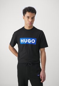 Zwarte katoenen T-shirt met een opvallende blauwe rechthoek met witte "HUGO" letters op de voorkant. Korte mouwen, ronde halsontwerp.