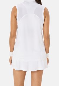 Vestido de tenis sin mangas blanco con un cuello alto, paneles de malla en la parte trasera y un dobladillo acampanado. Presenta un tejido ligero y acentos texturizados.