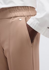 Μπεζ παντελόνι με υφή, διαθέτει ελαστική μέση και πλαϊνή τσέπη με μικρό μεταλλικό διακοσμητικό.
