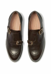 Ciemnobrązowe skórzane buty z podwójnym zapięciem, z detalami brogues wzdłuż krawędzi i gładką teksturą. Płaskie gumowe podeszwy.