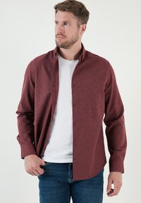 Camisa de botones burdeos hecha de tela texturizada, con un cuello clásico y mangas largas, combinada con una camiseta blanca de cuello redondo por debajo.