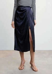 Gonna midi drappe in blu navy con spacco laterale e dettaglio legato, abbinata a una maglietta a maniche lunghe a strisce bianche e nere e sandali nudi.