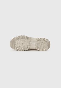 Beige sneaker sole with deep treads and pronounced rubber patterns. Features branding “GOODYEAR” near the heel. Textured for grip.