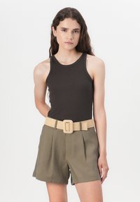 Ruda, raukšlių tankų marškinėliai derinami su alyvuogių žalumos šortais. Apranga turi platų smėlio spalvos diržą su dekoratyvine sagtimi.