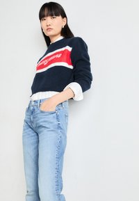 Knitted navy sweater with red and white stripes, featuring “tommy jeans” logo. Paired with light blue high-waisted jeans.