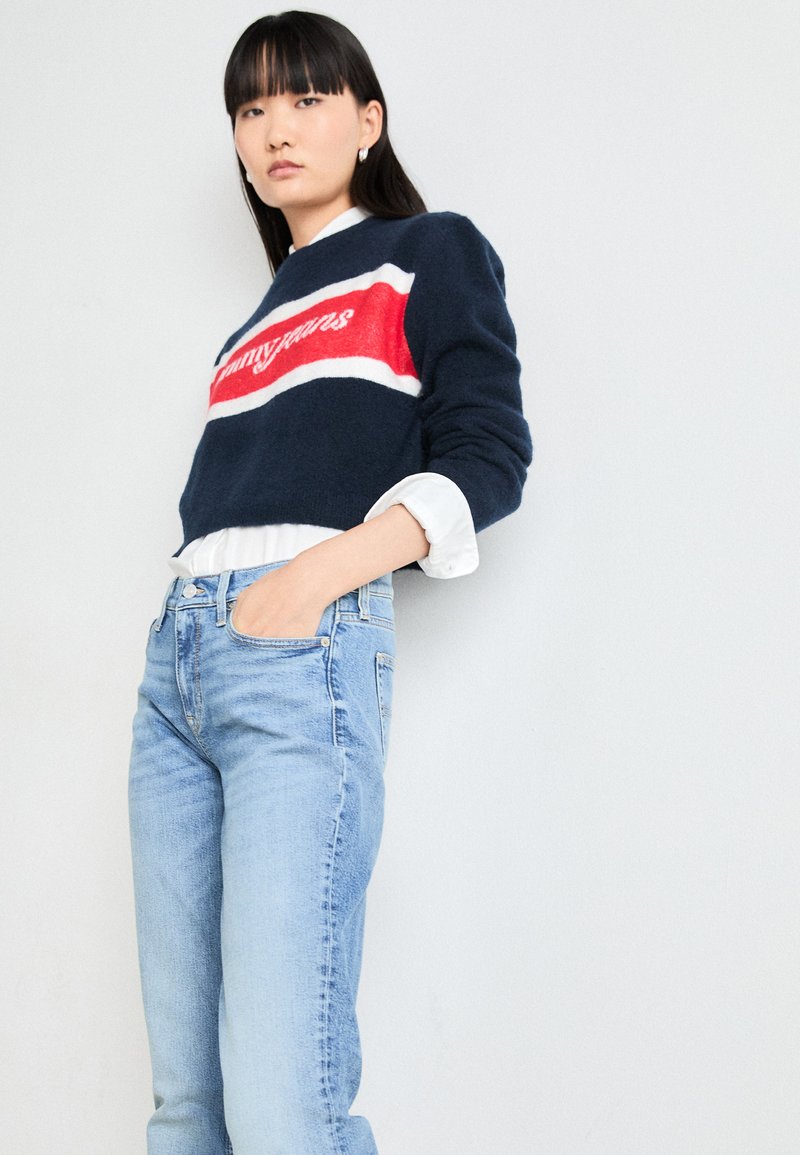 Dzianinowy granatowy sweter w czerwone i białe paski, z logo „tommy jeans”. W komplecie z jasnoniebieskimi spodniami z wysokim stanem.