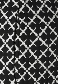 Svart och vit stickad tyg med ett sammankopplat X-mönster. Texturen verkar mjuk med ribbad finish längs kanterna.