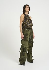 Top con collo halter in tessuto con stampa animale; pantaloni cargo larghi in tie-dye verde oliva con molteplici tasche e dettaglio a catena in vita.