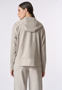 Felpa beige con cappuccio, vestibilità comoda e texture liscia. Presenta una tasca a marsupio e un orlo spaccato, abbinata a pantaloni coordinati.