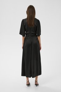 Melna satīna maksi kleita ar īsām pūkainām piedurknēm, piegulošu vidukli un plūstošu svārku. Uzmanību piesaista aizmugures centrāla šuve.