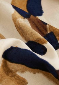 Tissu doux avec des motifs abstraits de coups de pinceau beige, marron et bleu foncé, montrant des plis et la texture en gros plan.