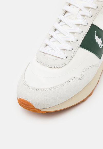 Λευκά αθλητικά παπούτσια με λείο δέρμα και σουέτ λεπτομέρειες, διαθέτουν πράσινη ρίγα στο πλάι και πορτοκαλί λάστιχο σόλα. Οι κορδόνες είναι λευκές.