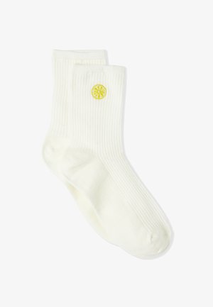 Calcetines blancos con canalé y un detalle de bordado de una rodaja de limón amarilla. Textura suave, longitud estándar hasta la pantorrilla, adecuados para uso casual.