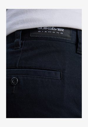 Donkerblauwe broek met een gestructureerde stof, een achterzak, een knoopsluiting en een zwart label met de tekst "Quiksilver Diamond."