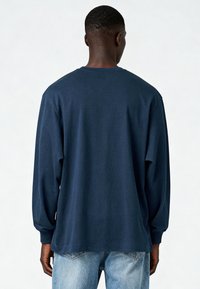 T-shirt à manches longues bleu marine avec une coupe décontractée et un col rond, doté de poignets côtelés et d'un tissu en coton lisse. Porté avec un jean bleu clair.