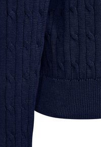 Marineblauwe gebreide trui met kabelpatroon en geribde zoom en manchetten, met detail van de mouw en onderrand.