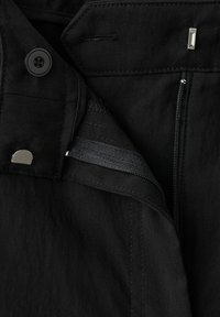 Tissu noir avec une fermeture éclair partiellement ouverte, un bouton et une fermeture à crochet métallique sur un pantalon ou un jean.